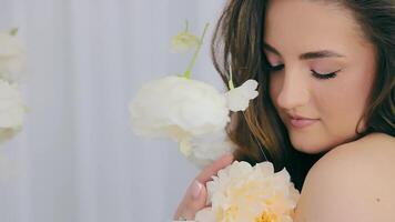 a menina abraços uma branco flor. uma cabelos escuros mulher suavemente carícias uma flor com dela mão e goza a beleza do flores feliz mulher video