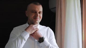 The man gets dressed and does his buttons on the sleeves of his white shirt. Action. Close up of male arms, man sitting and trying to button up. video