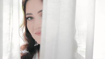 Close-up of the bride's face hiding behind a white curtain. Happy woman looking at the camera from behind the curtains video