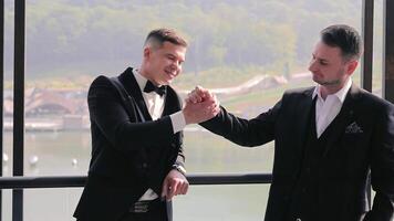 The groom stands on the balcony of the hotel with his friends. Stylish men in black jackets are talking to each other on their wedding day video