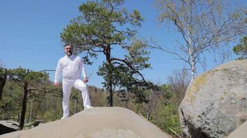 Masculin chanteur performant sensible chanson sur Haut de une Montagne dans le milieu de la nature. barbu chanteur dans vghite sirt en chantant et diffusion mains video