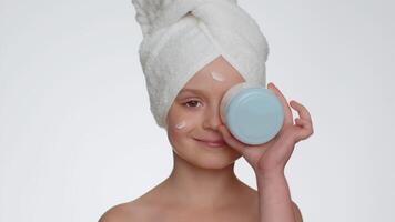 Jeune souriant enfant fille appliquant nettoyage hydratant crème, à la recherche à caméra en portant crème pot video
