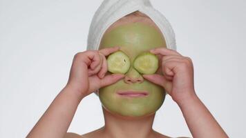 lindo sorridente criança menina criança dentro toalha em cabeça aplicando limpeza hidratante verde mascarar em face video