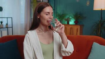 Thirsty one young woman sitting at home holding glass of natural aqua make sips drinking still water video