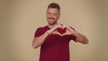 Smiling bearded handsome young man makes heart gesture demonstrate love sign expresses good feelings video