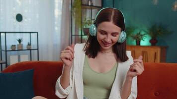 Happy relaxed girl in wireless headphones dancing listening favorite rock n roll music on home couch video