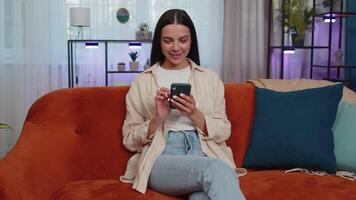 Portrait of adult girl sitting on sofa, using smartphone share messages on social media application video