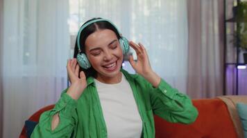 Happy relaxed girl in wireless headphones dancing listening favorite rock n roll music on home couch video