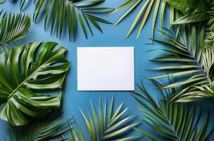 Blank Paper Surrounded by Tropical Leaves on Blue Background photo