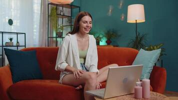 Woman sitting on home couch, looking at camera, making conference call with friends or family video