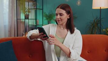 Portrait of adult girl sitting on sofa, using smartphone share messages on social media application video