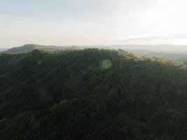 Soft rays of sunlight spill over forested hills, casting a warm glow on the lush landscape as evening approaches photo