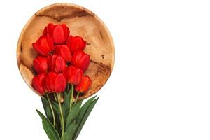 Red tulips with leaves lie on a wooden plate on a white background, horizontal with copy space photo