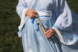 A woman in a traditional Chinese hanfu dress holds a bamboo flute close up photo