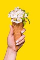 hielo crema hecho de flores en un gofre cono es retenida por un joven mujer en un amarillo antecedentes foto