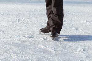 Men's legs in black skates close-up, standing on the rink facing the sun. Active winter holidays photo