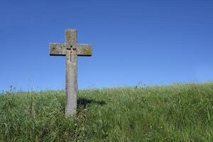 Cross made out of stone on a green grass field with the blue sky in the background photo