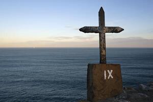 Metal cross in front of the ocean during sunrise photo