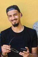 Close Up Portrait of Smiling Sudanese Teenager with Broad Smile, Chin, and Cap Using Smartphone photo