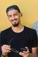 Close Up Portrait of Smiling Sudanese Teenager with Broad Smile, Chin, and Cap Using Smartphone photo