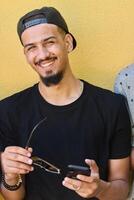 Close Up Portrait of Smiling Sudanese Teenager with Broad Smile, Chin, and Cap Using Smartphone photo