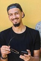 Close Up Portrait of Smiling Sudanese Teenager with Broad Smile, Chin, and Cap Using Smartphone photo