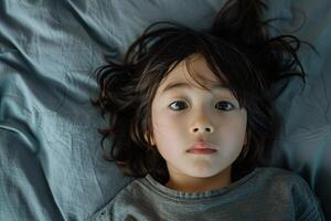 Portrait of a 10 year old Japanese child lying on the bed, looking at the camera from directly above, with scared face and gloomy mood photo