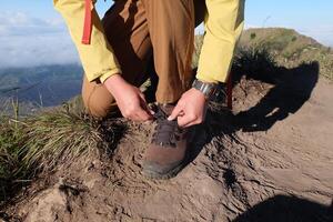 Hiker Tying Shoe on Mountain Peak Preparing for Adventure with Scenic View photo