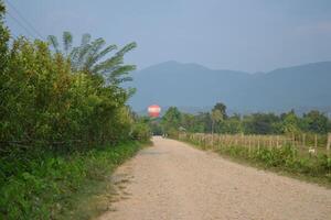 Hot air balloons pass high above the dusty dirt road photo