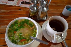 A bowl of rice in vegetable soup and a cup of tea are served on the table photo