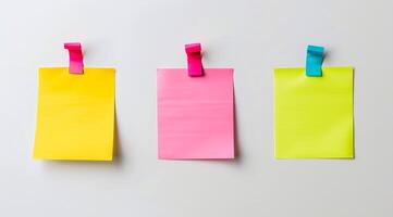 Three colourful post-it sticky notes are hanging on a white wall photo