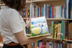 A young mother wearing a white tank top is flipping through a children's book in the bookstore photo