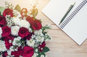 Notebook and pen on a wooden table With beautiful roses photo