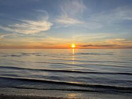 Orange sunset sky with clouds against the backdrop of ocean waves and the coast. Inspirational calm sea with sunrise sky. Colorful horizon above the water. photo