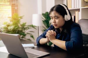 creative young student uses a laptop to complete online homework for college and university courses. Woman studies a book and conducts research for online academy using laptop in office. photo