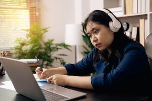 creative young student uses a laptop to complete online homework for college and university courses. Woman studies a book and conducts research for online academy using laptop in office. photo