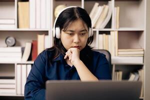 creative young student uses a laptop to complete online homework for college and university courses. Woman studies a book and conducts research for online academy using laptop in office. photo