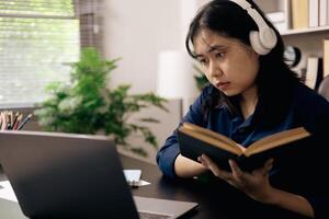 creative young student uses a laptop to complete online homework for college and university courses. Woman studies a book and conducts research for online academy using laptop in office. photo