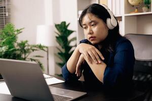 creative young student uses a laptop to complete online homework for college and university courses. Woman studies a book and conducts research for online academy using laptop in office. photo