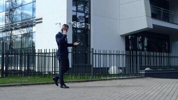 Businessman engaged in a call, phone to ear, strides confidently across the frame with an office building backdrop. Businessman conveys urgency as he walks. Businessman's dialogue reflects decisive video