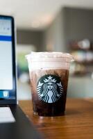 Samut Prakan, Thailand - May 25, 2024 Starbucks cold brew beverage cup on wood table with computer notebook. photo