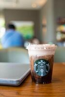 Samut Prakan, Thailand - May 21, 2024 Starbucks cold brew beverage cup on wood table with computer notebook. photo