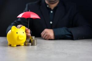 Businessman hand holding umbrella over coin stack and piggy bank. Financial Insurance, Protection photo