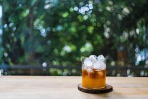 naranja jugo con negro café y mini redondo hielo cubitos en vaso en madera mesa foto