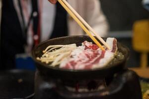 Hand using wood chopsticks grilled meat in hot pan photo