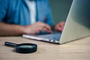 A businessman works on a computer with a magnifying glass on table. concept for analyzing data. Searching for information or evidence photo