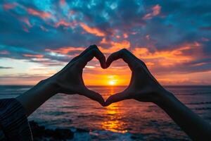 The person's hands are folded in the shape of heart and setting sun is in the center. Beautiful and romantic landscape photo