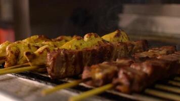 avvicinamento lento movimento metraggio di cucinando acquolina in bocca Maiale e pollo souvlaki torrefazione su un' barbecue. selettivo messa a fuoco video