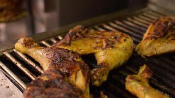 Close-up of grilled juicy chicken legs on the grill BBQ. Golden crispy skin chicken meat with spices on grid. Side view from above video