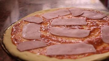 mãos vestindo Preto luvas spreads fatias presunto em uma pizza base com vermelho tomate molho. conceito do cozinhando delicioso pizza. degrau de etapa. degrau 4. meio tomada. lento movimento video